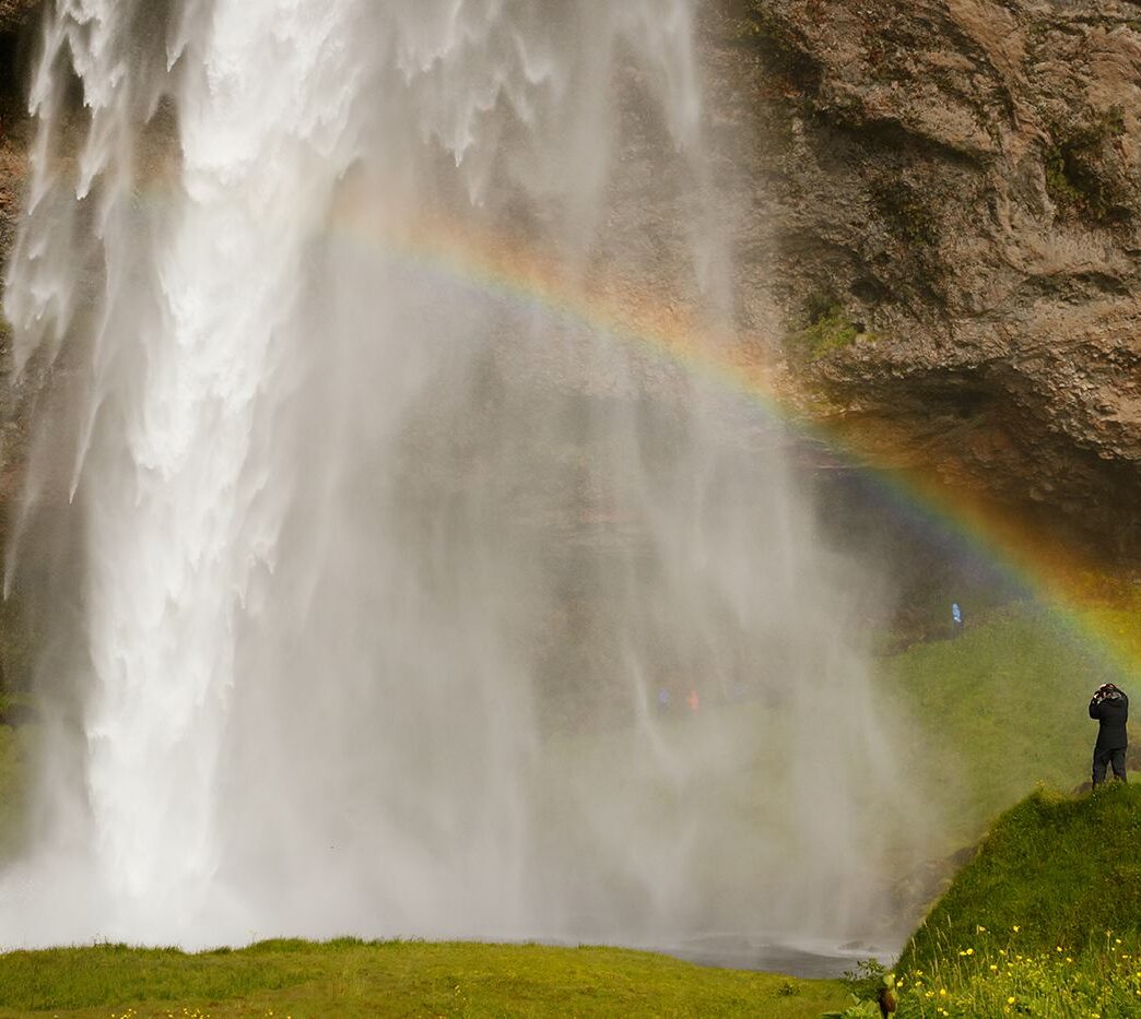 Człowiek, wodospad i tęcza, Seljalandsfoss, Islandia