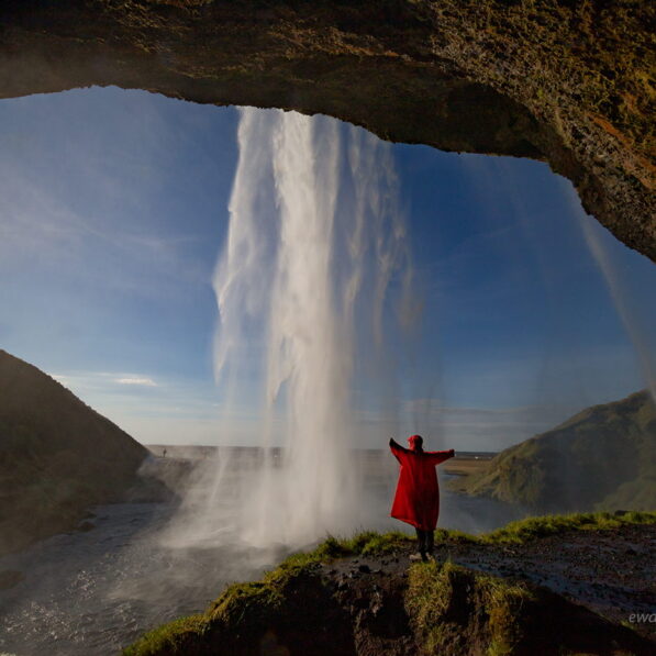 Za wodospadem Seljalandsfoss, Islandia, czerwona peleryna, człowiek za kaskadą wody, fotowyprawa